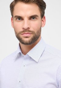 Camicia bianca con un sottile motivo a griglia blu navy, colletto button-down e bottoni a contrasto. Tessuto liscio con una vestibilità sartoriale.