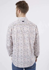 Chemise à manches longues en tissu crème avec un motif de feuilles multicolores. Elle présente un col et une étiquette au dos du col.