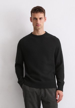Zwart gebreid sweater met een geribbelde structuur, ronde halslijn en lange mouwen. Gecombineerd met grijze corduroy broek.