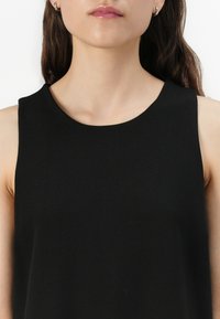 Svart ärmlös topp med ett mjukt, lätt tyg, hög rund halsringning och minimalistisk design. Inga synliga mönster eller accentfärger.