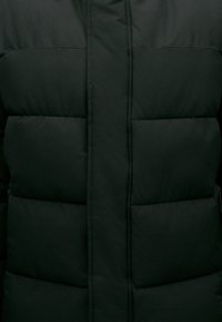 Chaqueta de plumas negra con costuras horizontales y una textura suave. Presenta un collar alto, bolsillos con cremallera y un cierre frontal con cremallera.