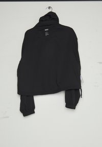 Sort hættetrøje med elastiske manchetter hængende på vægkrog, viser bagudsigt og hvid label nær kraven.