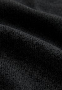 Gros plan sur un tissu tricoté noir et doux avec un tissage fin et texturé et des plis subtils créant lumière et ombre.