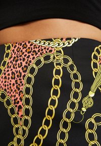 Jupe noire avec un design audacieux rose vif et imprimé léopard, agrémentée de motifs et accents en chaîne dorée, mettant en valeur la texture lisse du tissu.