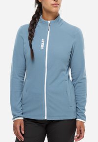 Veste en polaire bleu clair avec fermeture éclair sur le devant, col haut et accents blancs. Présente un tissu texturé et deux poches latérales.