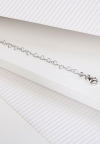 Silberne, herzförmige Kettenarmband mit einem Karabinerverschluss, das abwechselnde Glieder und eine glatte, polierte Oberfläche auf einem weißen Hintergrund aufweist.