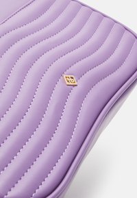 Borsa viola in pelle trapuntata con cuciture ondulate e piccolo dettaglio logo dorato. Texture liscia con forma strutturata.