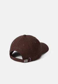 Casquette de baseball en coton brun avec un strap ajustable, présentant une couronne arrondie, des trous de ventilation cousus, et un logo en relief à l'arrière.