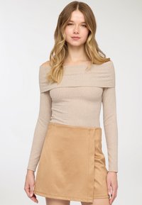 Top beige a coste con scollo a barca abbinato a una minigonna in raso color cognac con design avvolgente laterale, texture liscia e linee pulite.