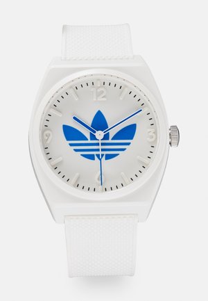 Montre blanche avec bracelet texturé, logo Adidas trefoil bleu sur le cadran, couronne argentée et aiguilles blanches pour les heures, minutes et secondes.