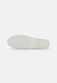 Hvit sneaker såle med et teksturert, rillert mønster for grep, flat form og minimalistisk design. Størrelseslabel synlig på sålen.
