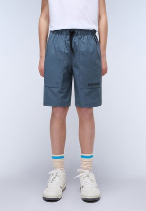 Blauwe, knie-lange shorts met een aantrekkoord in de taille, twee grote voorzakken en een logo-opdruk aan de zijkant, gecombineerd met witte sneakers en gestreepte sokken.