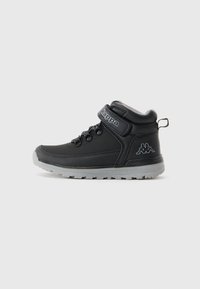 Zapatilla alta negra con suela gris, tirador, ganchos para cordones y tira de velcro con la marca "Kappa" sobre un fondo blanco liso.