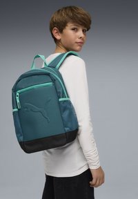 Sac à dos turquoise avec base noire, doté d'une poche avant texturée et de panneaux latéraux en mesh. Comprend des bretelles rembourrées et une poche zippée à l'avant.