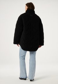 Zwarte gewatteerde oversized jas van zachte fleece met een hoge kraag. Gepaard met lichtblauwe flared jeans. De stof heeft een gestructureerde uitstraling.