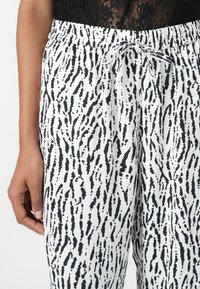 Pantaloni a righe bianche e nere con vita regolabile. Il tessuto presenta una texture che ricorda le pennellate, evidenziando una vestibilità ampia.