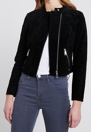 Černá semišová bunda s stojáčkovým límcem, zipem vpředu a dvěma bočními kapsami. Kombinováno se šedými slim fit džíny a bílým topem.