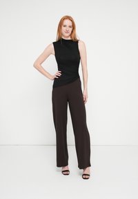 Μαύρο αμάνικο τοπ με ραντάκια και ραβδώσεις συνδυασμένο με καφέ φαρδιά παντελόνια με ελεύθερη ροή· λεία υφή, μινιμαλιστικό στυλ και μαύρα πέδιλα με ανοιχτά δάχτυλα.