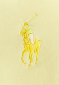 Gul polo skjorta med en texturerad tyg. Har en broderad bild av en polospelare i gula nyanser på hästryggen.