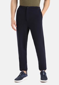 Mörkblå sweatpants i mjukt tyg med elastiskt midjeband, knappstängning och tapered design. Matchade med mörka sneakers.