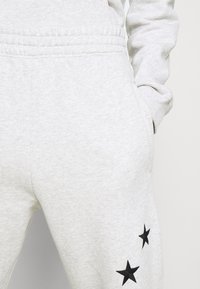 Ljusgråa mjukisbyxor i mjukt tyg med elastisk midja och tre svarta stjärnmönster på nedre vänstra benet.