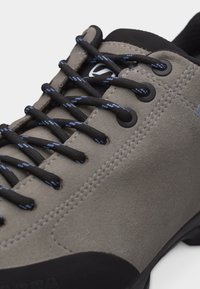 Κοντινή λήψη γκρι suede πεζοπορικού παπουτσιού με μαύρα και μπλε κορδόνια, μεταλλικά κορδόνια και μαξιλαρωμένο γιακά.