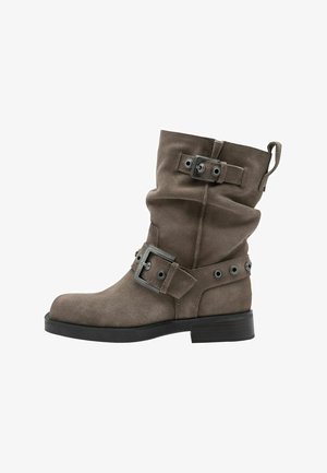 Ruskeat mokkanahkasaappaat nilkkapituisella, löysällä muotoilulla, solkikoristeilla, metallikomponenteilla, rei'illä ja matalalla puolella. Sileä pinta.