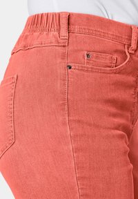 Koraalroze jeans met een elastische tailleband, met een klassieke vijf-pocketstijl en subtiele stiksels. Gladde denimtextuur.