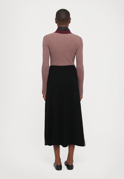 Person standing with back facing the camera wearing a mauve long-sleeve top, black midi skirt, and black flats on a white background.