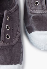 Zapatillas de lona grises con suelas de goma blanca, que presentan ojales de plata y detalles de costura. Vista en primer plano que resalta la textura y el diseño.