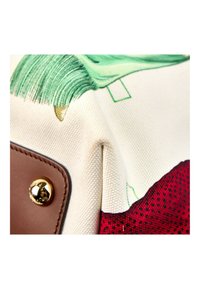 Coin d'un sac en tissu avec un motif imprimé vert et rouge, un patch en cuir beige et un clou métallique rond doré.