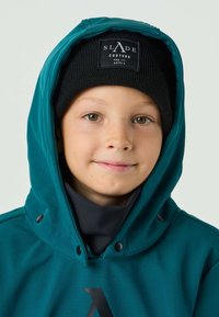 Giacca con cappuccio color verde acqua con dettagli neri e logo, indossata sopra un scaldacollo nero. Berretto a maglia nero con etichetta. Tessuto dalla texture liscia.