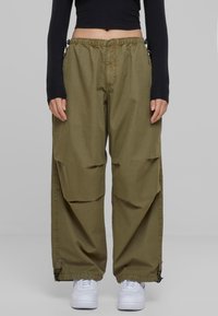 Olivové cargo kalhoty s elastickým pasem, bočními kapsami a nastavitelnými manžetami. Nosené s bílými teniskami a černým topem s dlouhým rukávem.