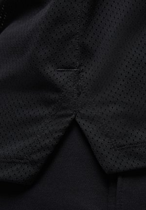 Schwarzes Sportshirt aus einem mesh ähnlichen Material mit kleinen Perforationen, akzentuiert durch einen glatten, einfarbigen Stoff darunter. Dezente Nahtdetails sind sichtbar.