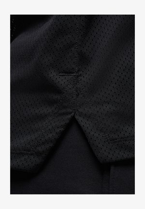 Camiseta atlética negra con una textura de malla con pequeñas perforaciones, acentuada por una tela sólida y suave debajo. Detalle de costura sutil visible.