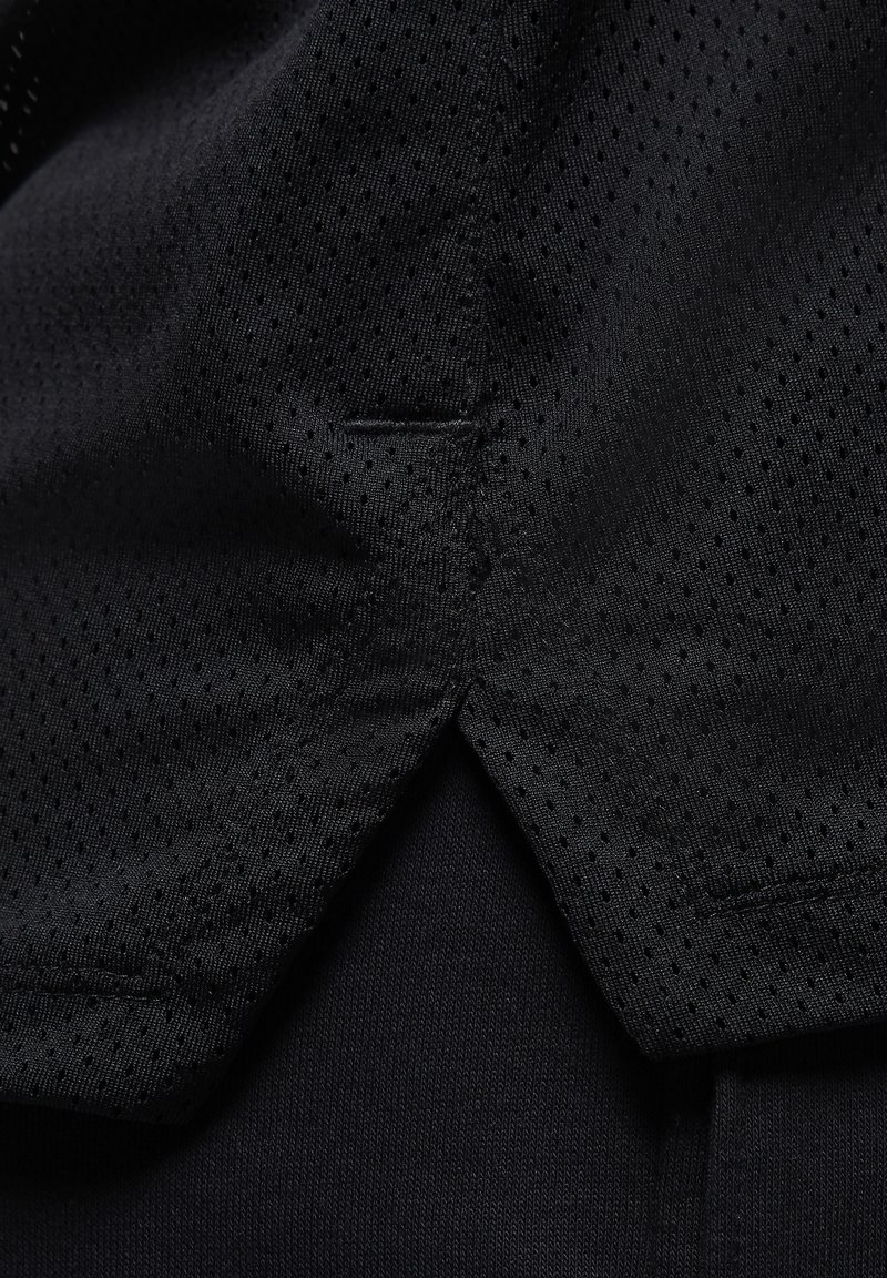 Schwarzes Sportshirt aus einem mesh ähnlichen Material mit kleinen Perforationen, akzentuiert durch einen glatten, einfarbigen Stoff darunter. Dezente Nahtdetails sind sichtbar.