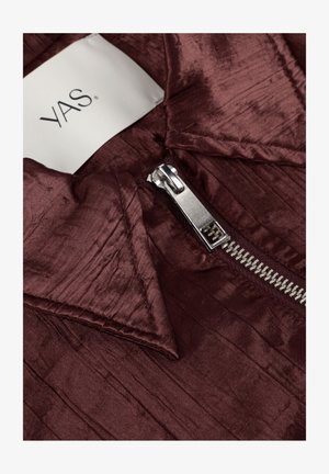 Close-up of metallic zipper on textured deep burgundy fabric with a white clothing label marked "YAS."