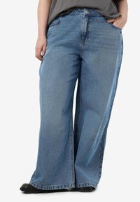 Wide-leg blue denim jeans with a mid-rise waist, featuring front pockets and a straight cut. The fabric has a soft texture with a faded finish.