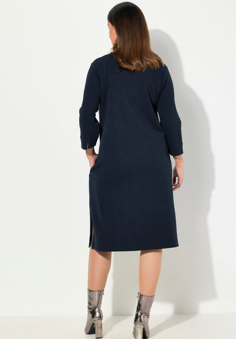 Námořnická modrá šaty s dlouhými rukávy a postranními rozparky, vyrobené z texturované látky, spárované s metalickými kotníkovými botami.