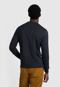 Marineblaues Langarmshirt mit Rundhalsausschnitt, aus leichtem Stoff gefertigt, zeichnet sich durch eine glatte Textur und einfaches Design aus; kombiniert mit Cordhosen.