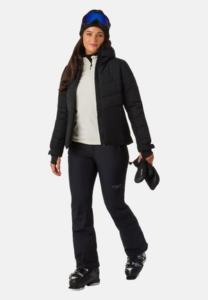 Schwarz isolierte Jacke mit Kapuze, helles Langarmshirt, schwarze Skihose und Skischuhe. Zubehör umfasst Skibrille und Handschuhe.