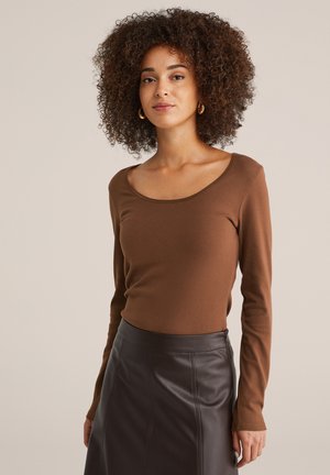 Bruine top met lange mouwen en een ronde halslijn, gecombineerd met een zwarte leren rok met verticale naden en een getailleerde taille.