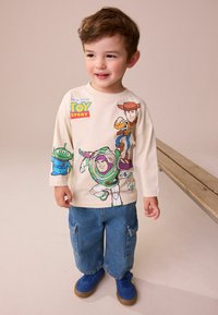 Světle béžová košile s dlouhým rukávem, na které je animovaný Buzz Rakeťák, Woody a mimozemšťan, zkombinovaná s džínovými cargo kalhotami a modrými teniskami.