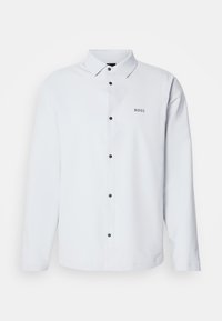 Chemise blanche à manches longues avec des boutons noirs et un col, avec le mot "BOSS" imprimé sur la poitrine gauche.