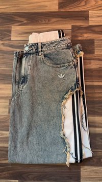 Διπλωμένα σορτς από ανοιχτού χρώματος denim με φθαρμένες άκρες, στρωμένα πάνω σε λευκό κολάν με μαύρες κάθετες ρίγες, τοποθετημένα σε ξύλινο πάτωμα.
