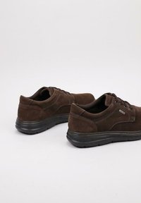 Chaussures en daim marron avec semelles en caoutchouc noir, présentant un design discret, une fermeture à lacets et un détail de couture subtil.