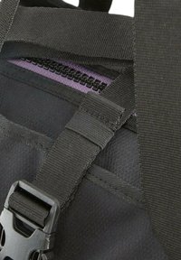 Musta kangaskassi, jossa on violetti vetoketju, nylonstrapsit ja muovinen solki, teksturoitu pinta ja yksityiskohtainen ompelu.