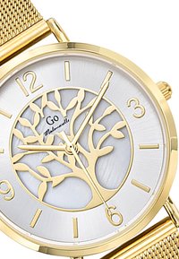 Montre dorée avec un cadran argenté arborant un design d'arbre. Bracelets en maille, marqueurs d'heures minimalistes et aiguilles discrètes.