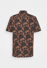 Chemise marron à manches courtes avec motif de rose et de feuille noire vue de dos sur fond blanc.