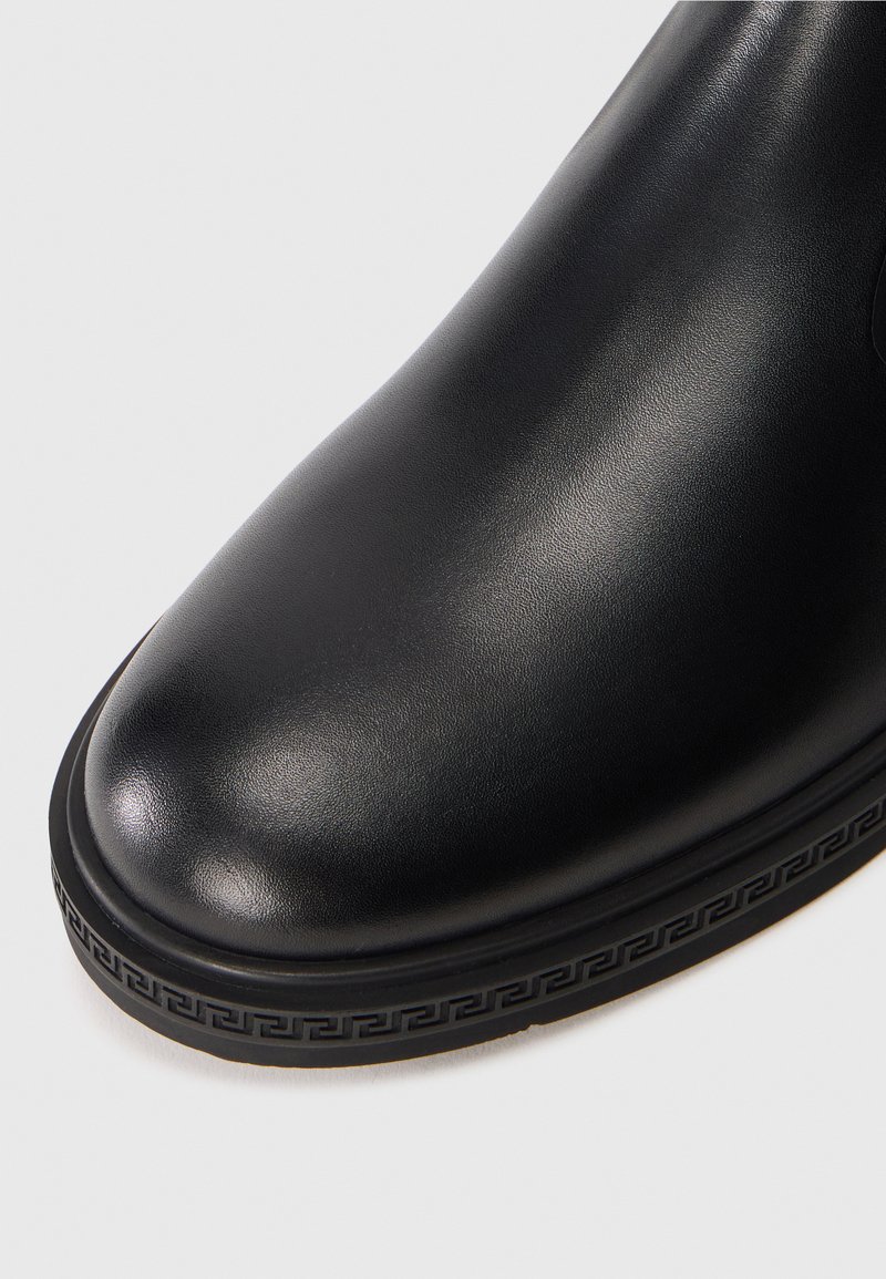 Punta di stivale in pelle nera con suola testurizzata che presenta un motivo decorativo a chiave greca lungo il bordo.